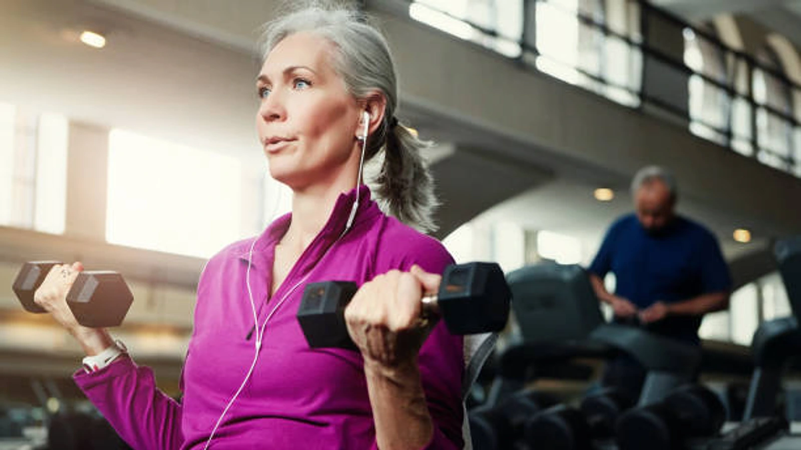 Mujer madura realizando un ejercicio de fuerza con mancuernas en el gimnasio